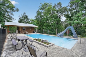 A swimming pool with a slide, picnic tables, and a covered seating area.