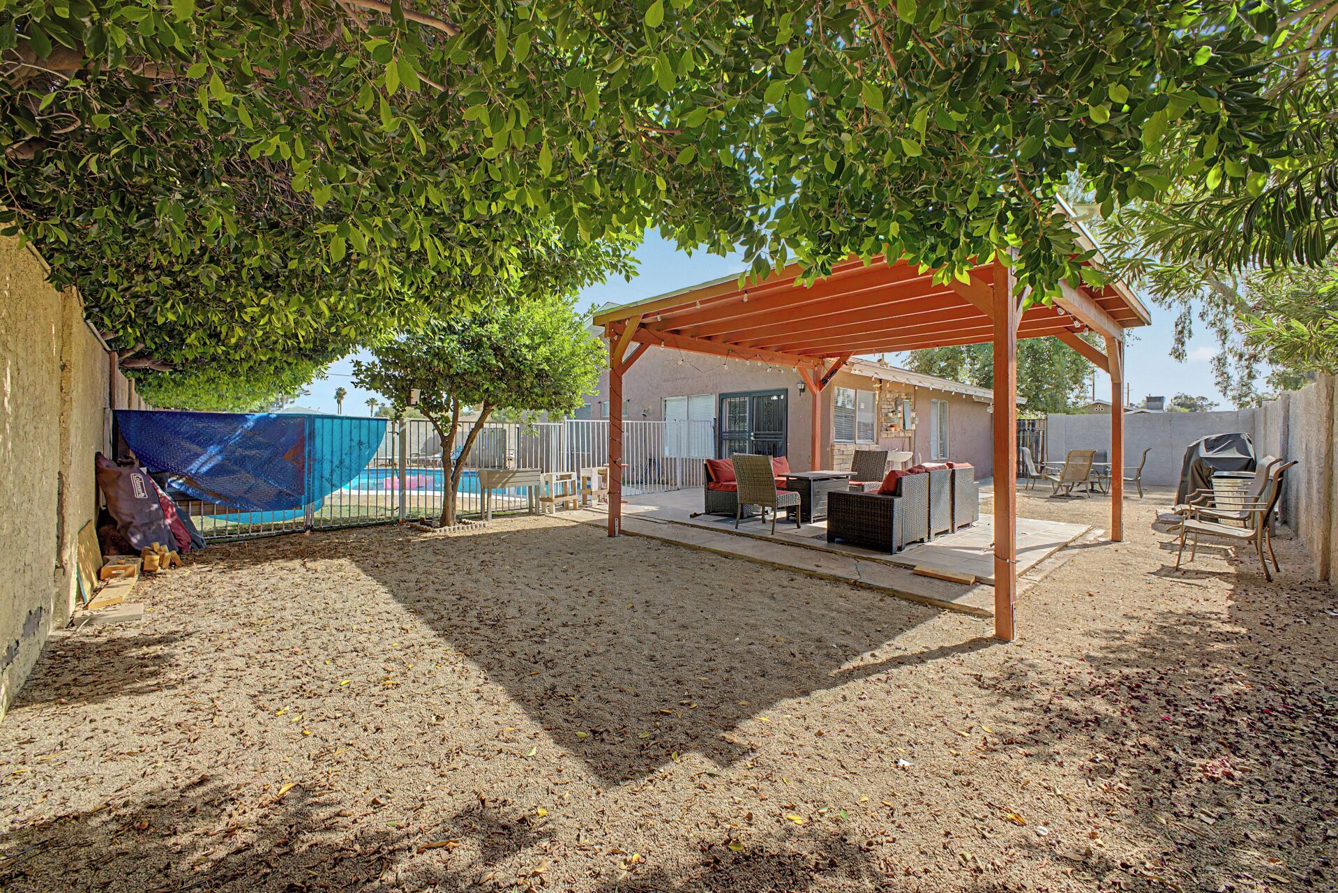 A covered outdoor seating area with a pool in the background.