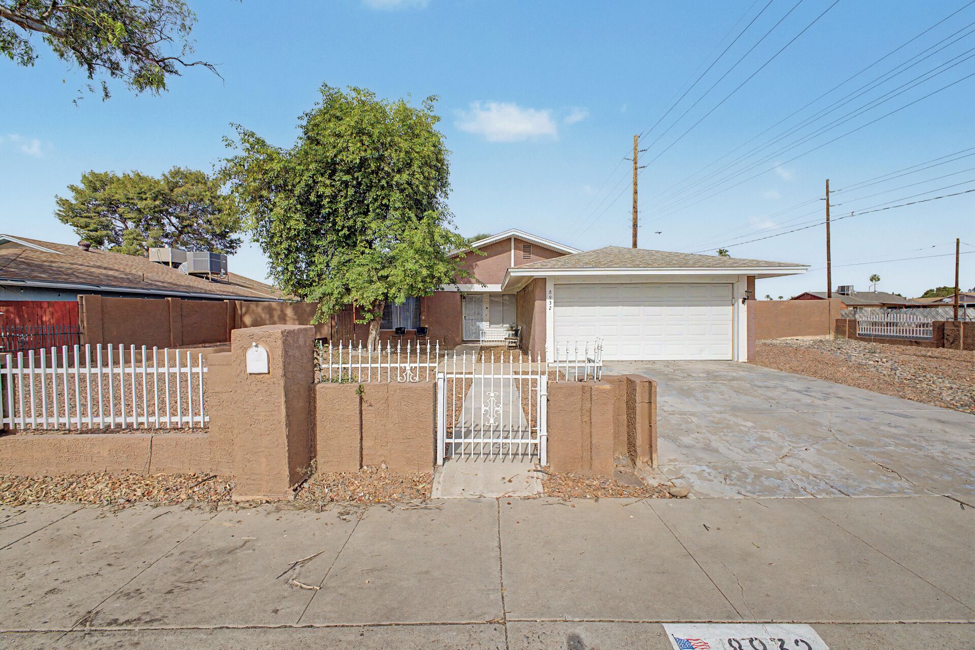 Um imóvel residencial com garagem, entrada com cerca e uma árvore.