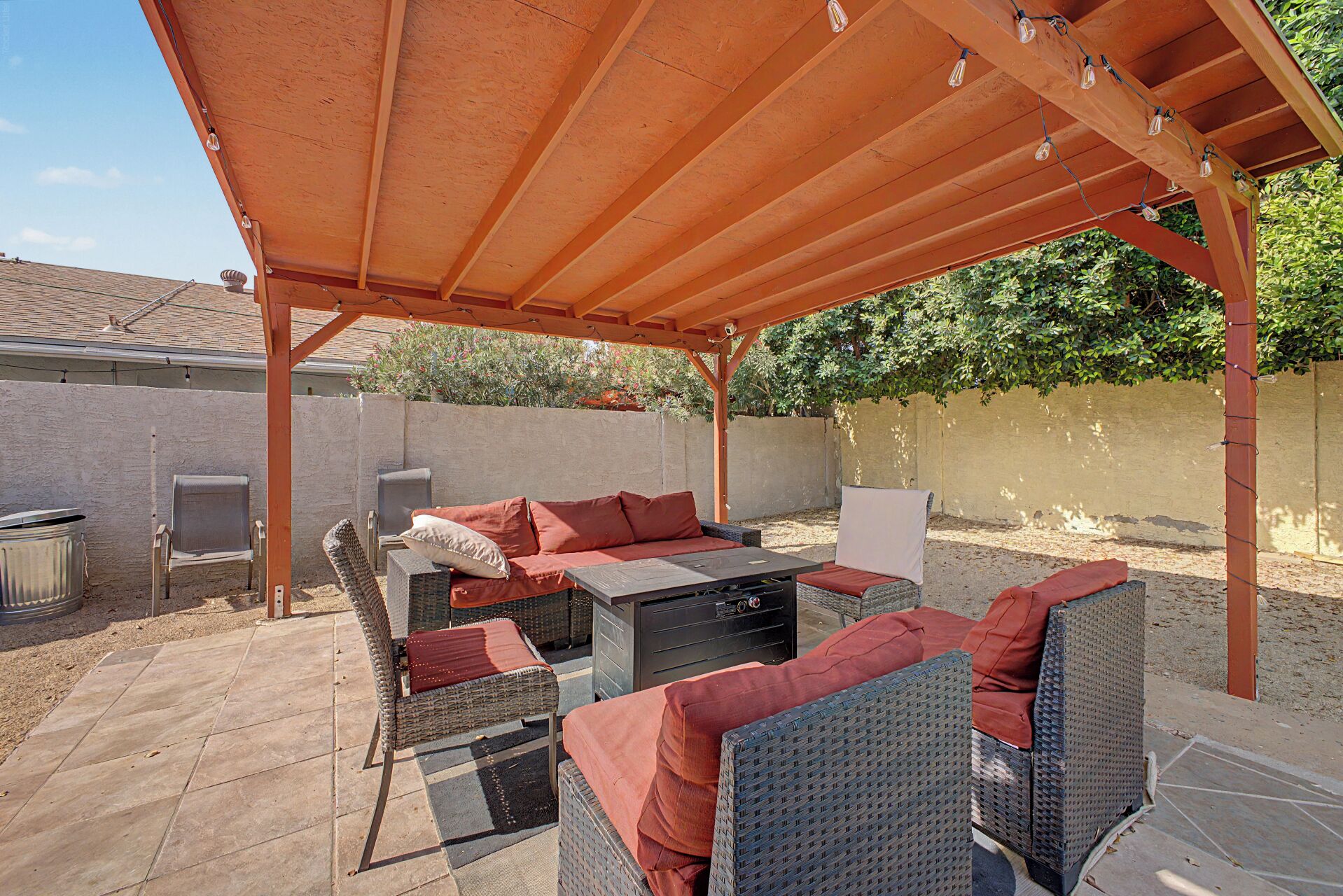 Terrassa exterior amb mobiliari de vimet, una barbacoa i una zona coberta amb llums de garlandes.