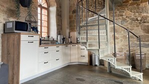 A kitchen with a stone wall, a white cabinet, a microwave, and a staircase with baskets. - Duplex Flat With a Fireplace in a Historic Vaulted Building (Grossharthau)