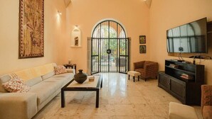 A living room with a sofa, coffee table, TV, and a large window with a view. - Chez David magnificent colonial retreat (Mérida)