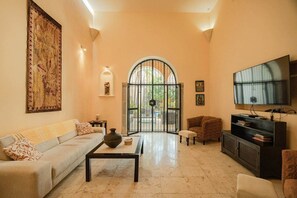 A living room with a sofa, coffee table, TV, and a large window with a view. - Chez David magnificent colonial retreat (Mérida)