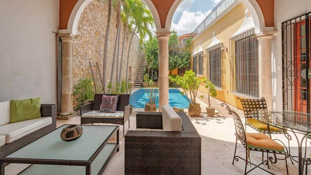 A covered outdoor area with a pool, seating, and a stone wall. - Chez David magnificent colonial retreat (Mérida)
