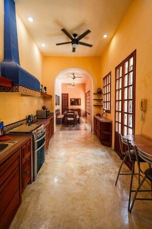A kitchen with a central island, a dining area with chairs, and a ceiling fan. - Chez David magnificent colonial retreat (Mérida)