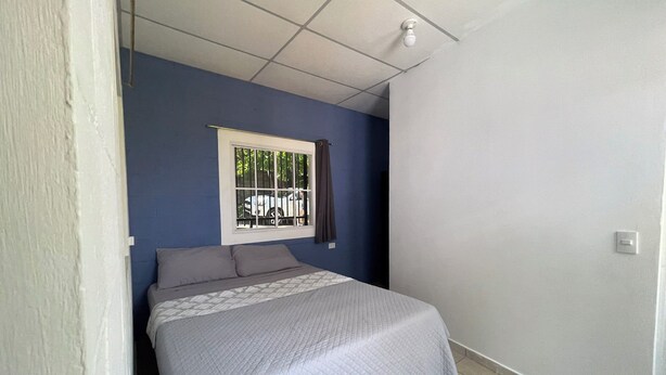 Una camera da letto con un letto, una finestra con grate, una lampada a soffitto e un interruttore a muro.