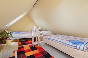 Una habitación pequeña y triangular con dos camas, un escritorio y una planta.