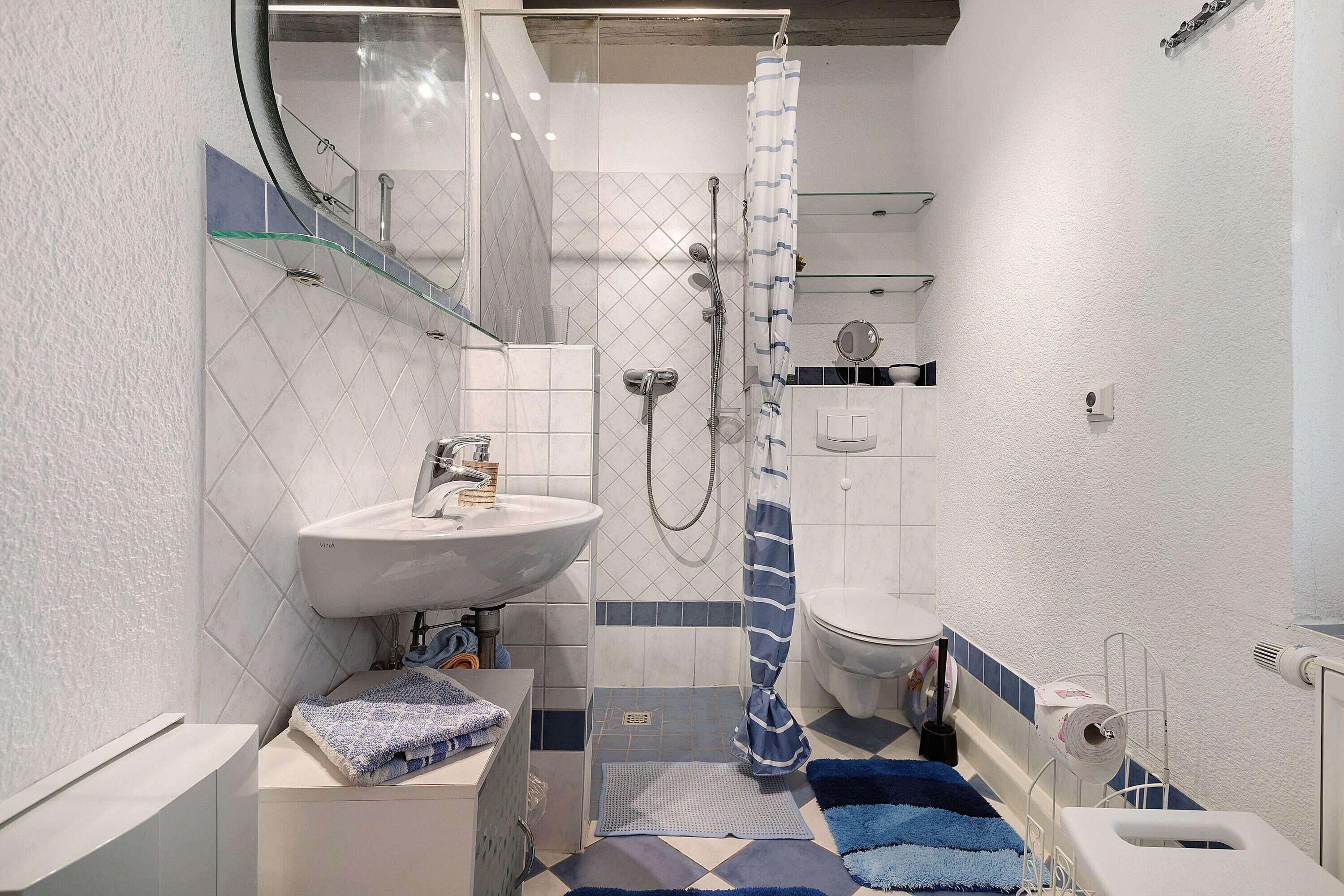 Ein Badezimmer mit weißem Waschbecken, Toilette, Dusche mit blauen und weißen Streifen und einem blauen und weißen Teppich auf dem Boden.