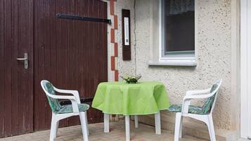 Ein kleiner Sitzbereich im Freien mit einem Tisch und zwei Stühlen, einer Tür und einem Fenster.