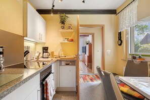 A compact kitchen with a dishwasher, coffee maker, and a small dining area with a chair and table. - Haus Schöne in Lebbin for 6 Guests (49 m²) (Groß Teetzleben)