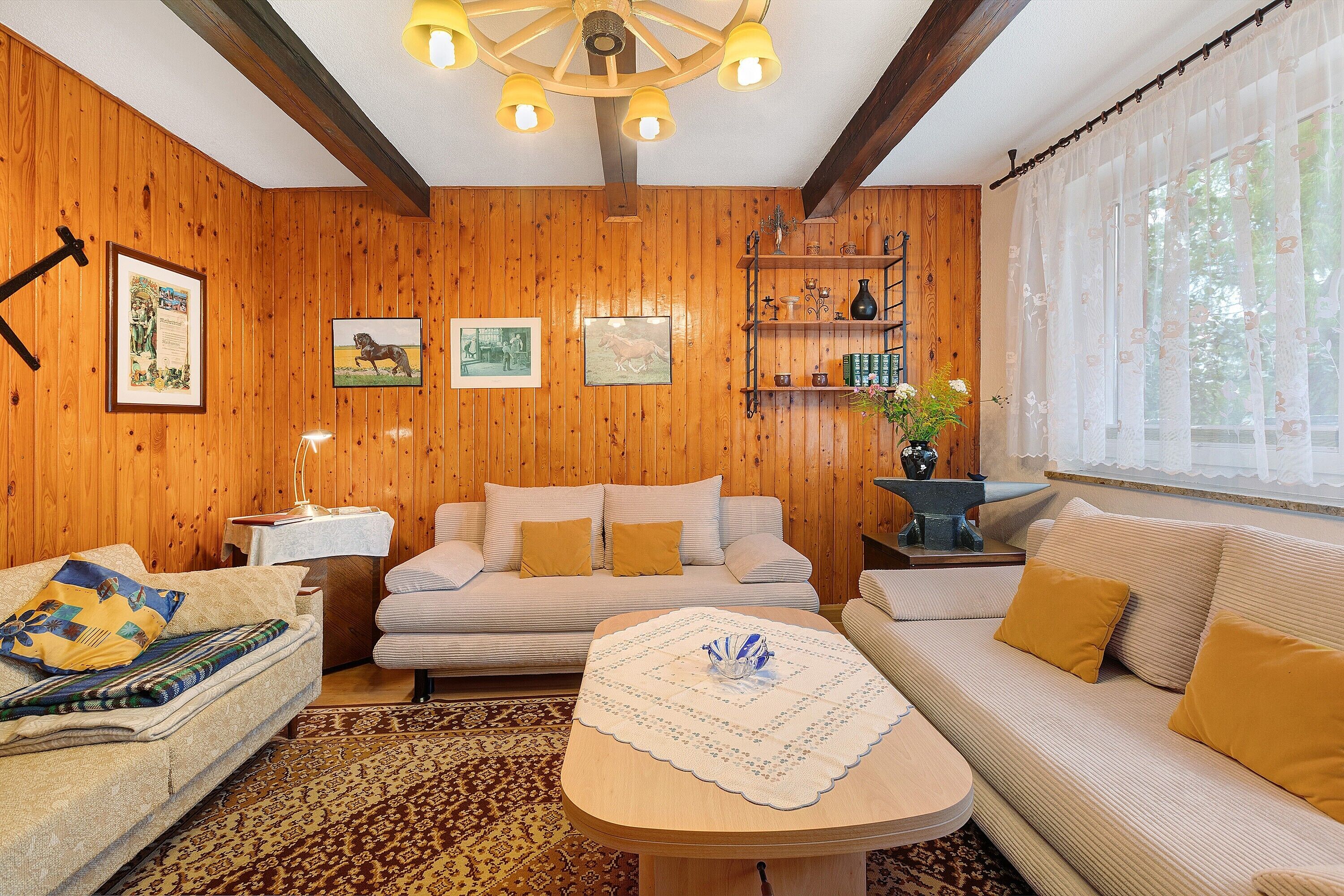 Ein gemütliches Zimmer mit Holzwänden, einem Bett, einem Sofa, einem Tisch und einem Fenster mit durchsichtigen Vorhängen.
