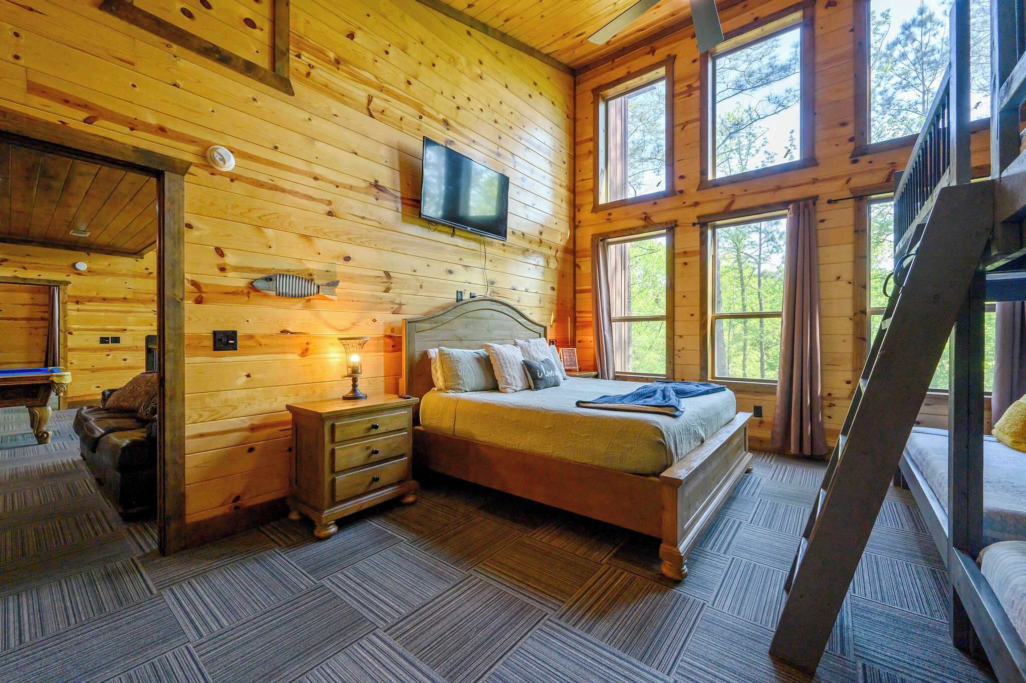 Ein Schlafzimmer einer Holzhütte mit Bett, Nachttisch, Schminktisch und einem an der Wand montierten Fernseher.