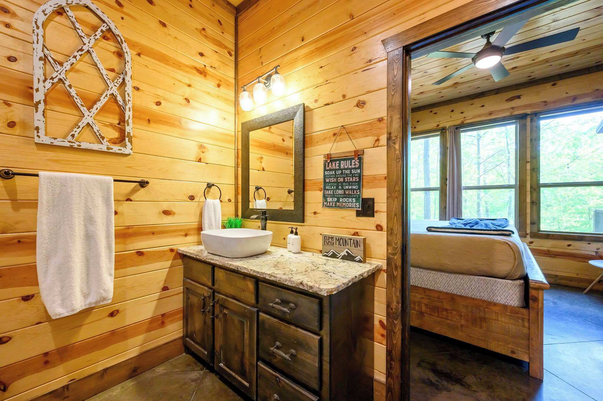 Een houten badkamer in een chalet, met een wastafel, spiegel, handdoekhouder, en een bord met de tekst 'LAKE RULES' en 'ALPINE MOUNTAIN'.