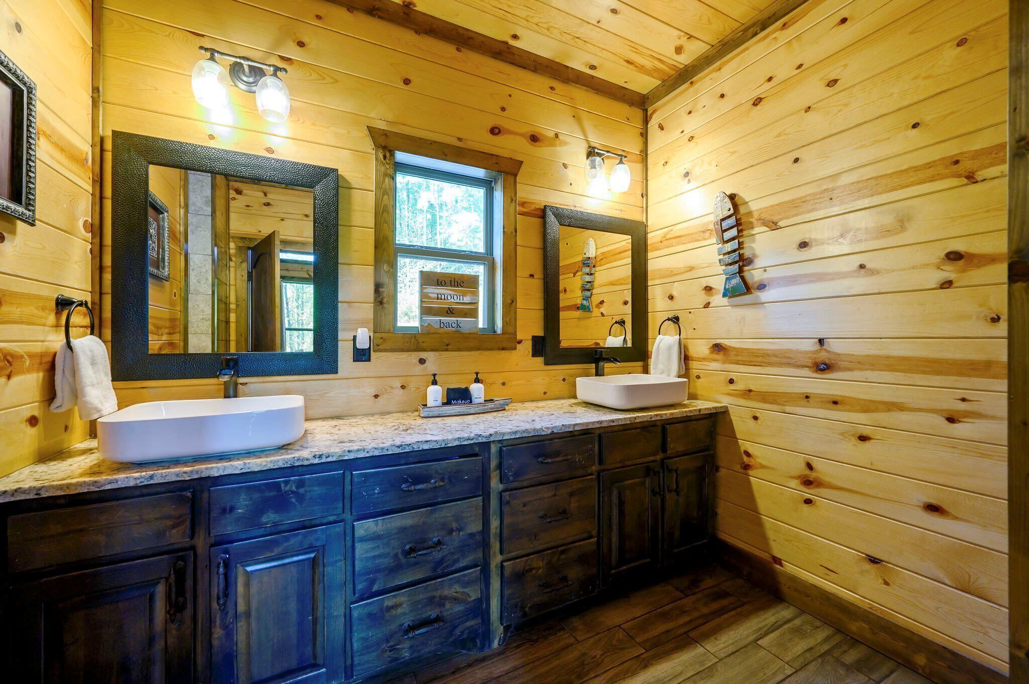 A wooden cabin bathroom with two sinks, dark cabinets, and a large mirror.
