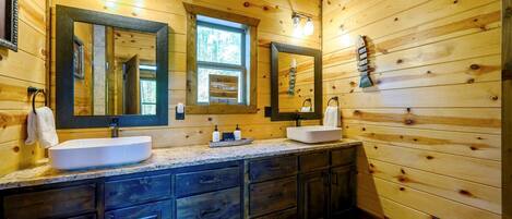 A wooden cabin bathroom with two sinks, dark cabinets, and a large mirror.