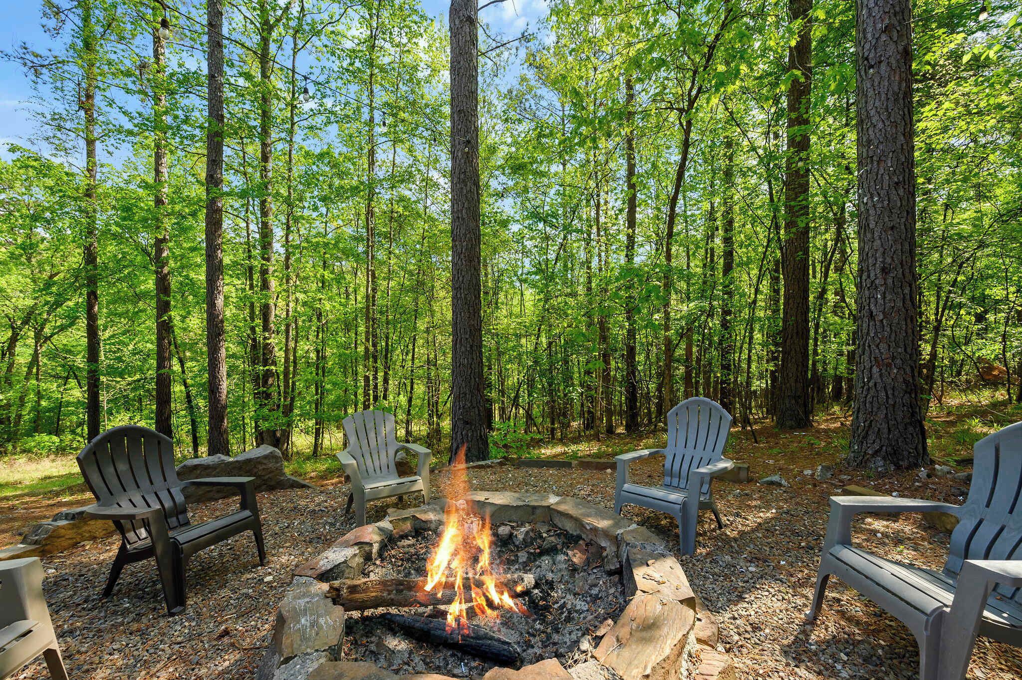 Un entorno boscoso con una hoguera y sillas Adirondack.
