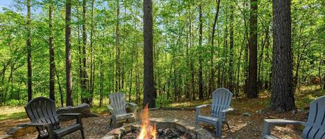 Un entorno boscoso con una hoguera y sillas Adirondack.