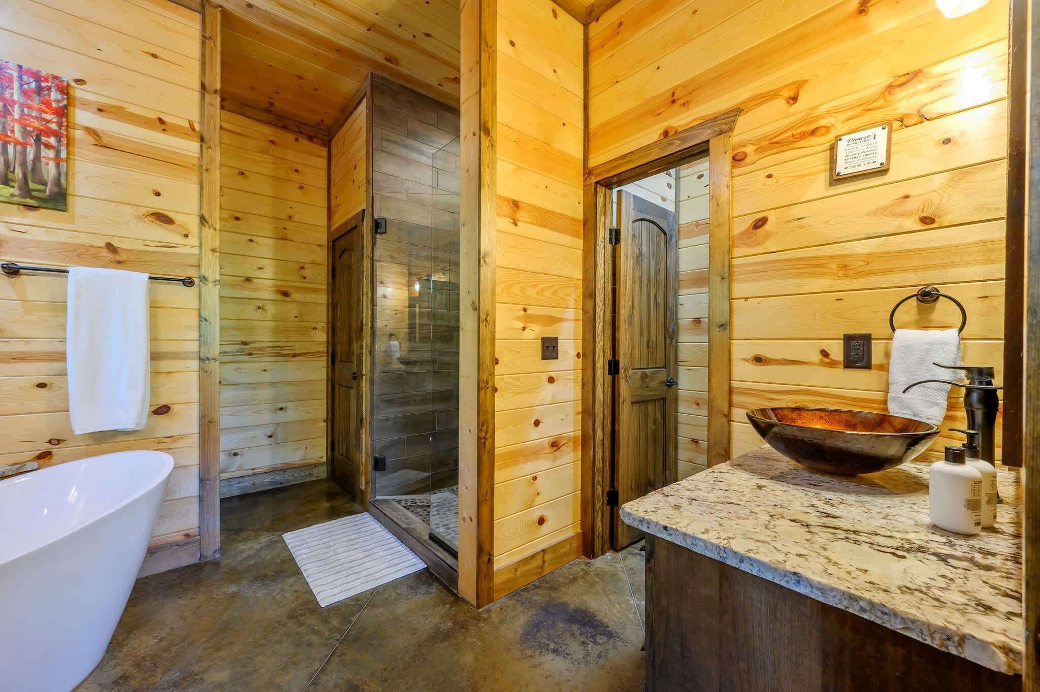 Baño de cabaña de madera con ducha de vidrio, bañera blanca y encimera de mármol.