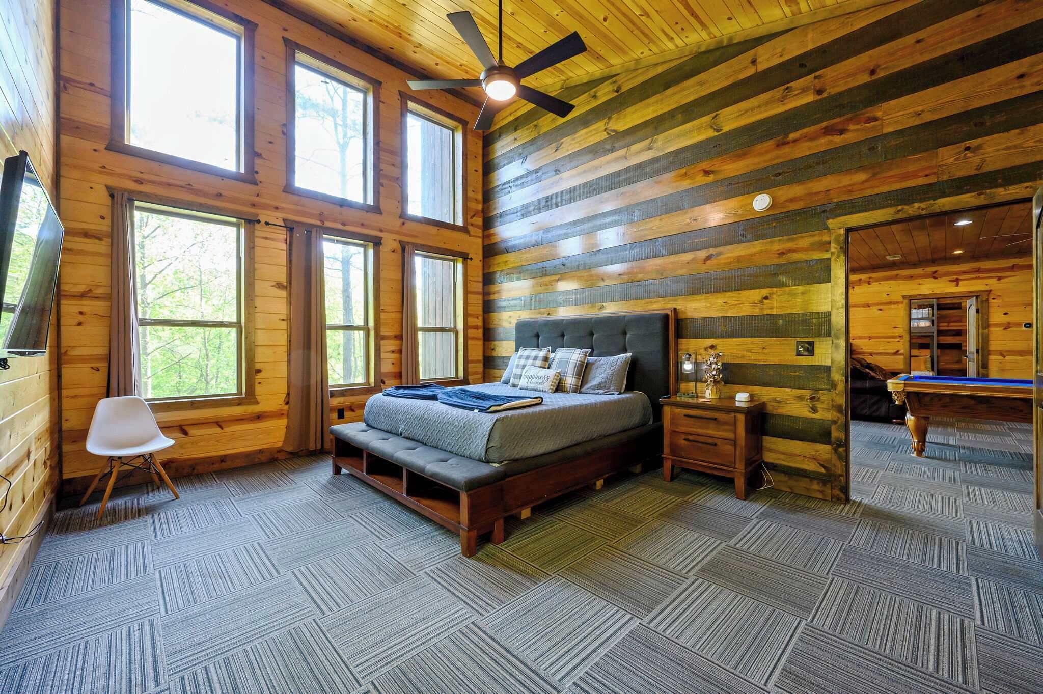 A log cabin bedroom with a bed, a chair, a ceiling fan, and a billiards table.