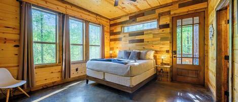 A wooden cabin bedroom with a bed, a ceiling fan, and large windows.