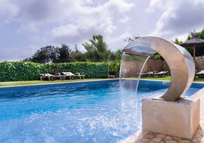 A swimming pool with a water feature, lounge chairs, and a hedge in the background. - Carob Tree House - Paderne, Albufeira (Albufeira)