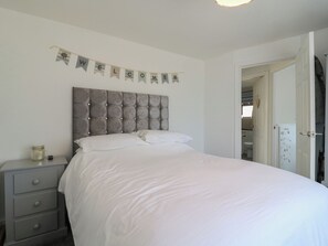 A bedroom with a bed, a nightstand, a wall-mounted welcome banner, and an open door leading to a bathroom. - 38 St Margarets (Dover)