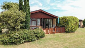 A single-story house with a red roof, a fenced yard, and a variety of greenery including a large bush and a tree. - 38 St Margarets (Dover)