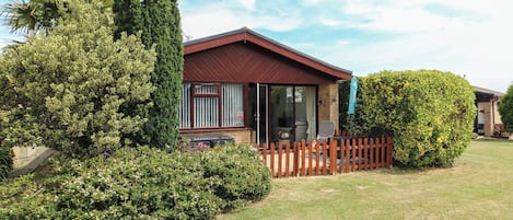 A single-story house with a red roof, a fenced yard, and a variety of greenery including a large bush and a tree.