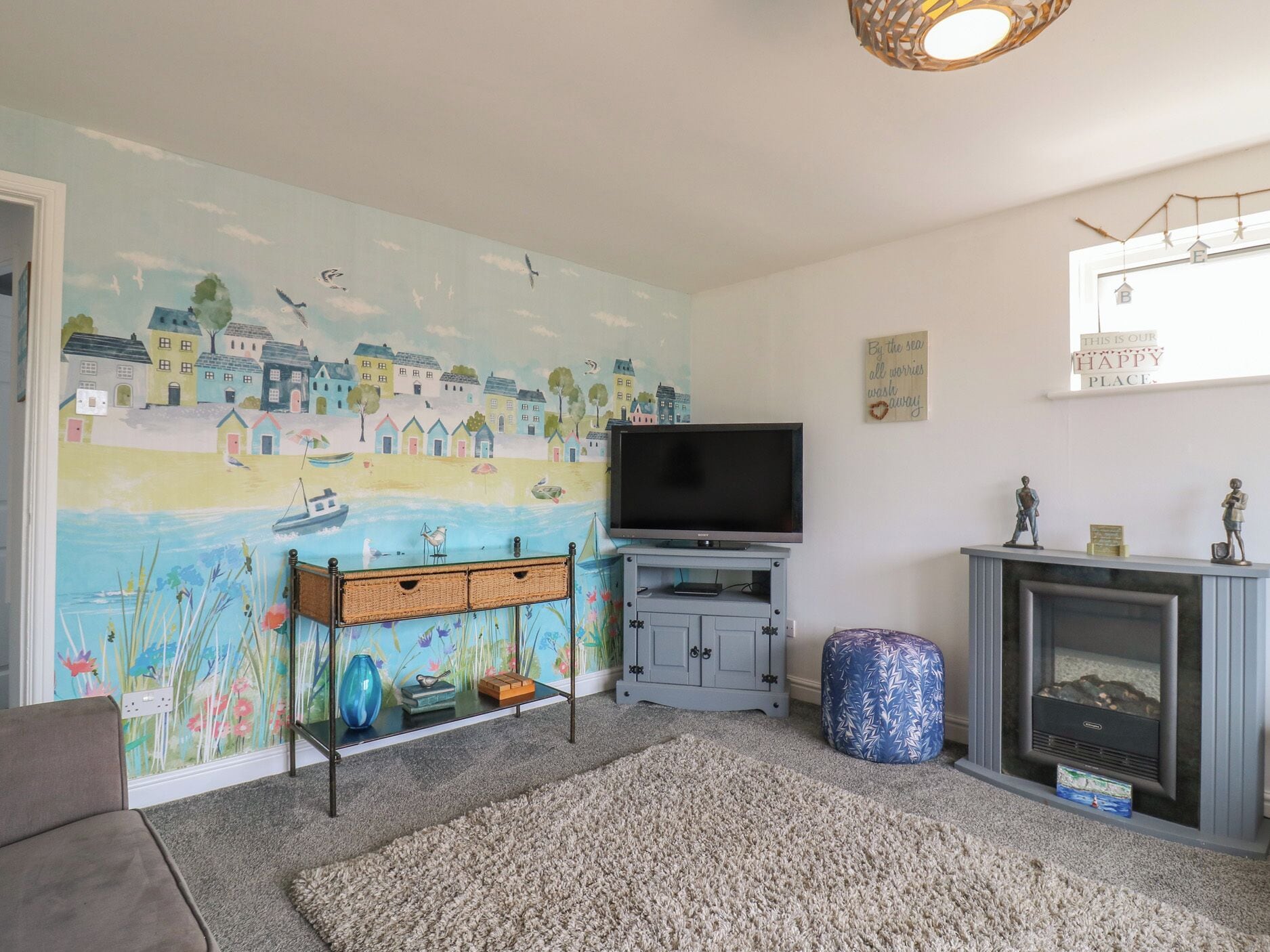 A living room with a mural, a flat-screen TV, a fireplace, and a cozy seating area.