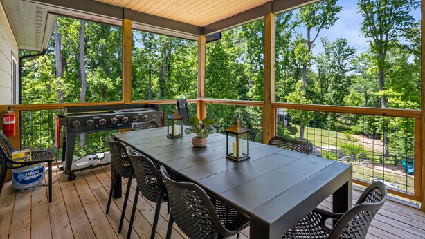 An outdoor deck with a grill, dining table, chairs, and a view of the surrounding forest. - Fox Den | 4 Suite Retreat + EV | 10 Mins to AVL (Asheville)