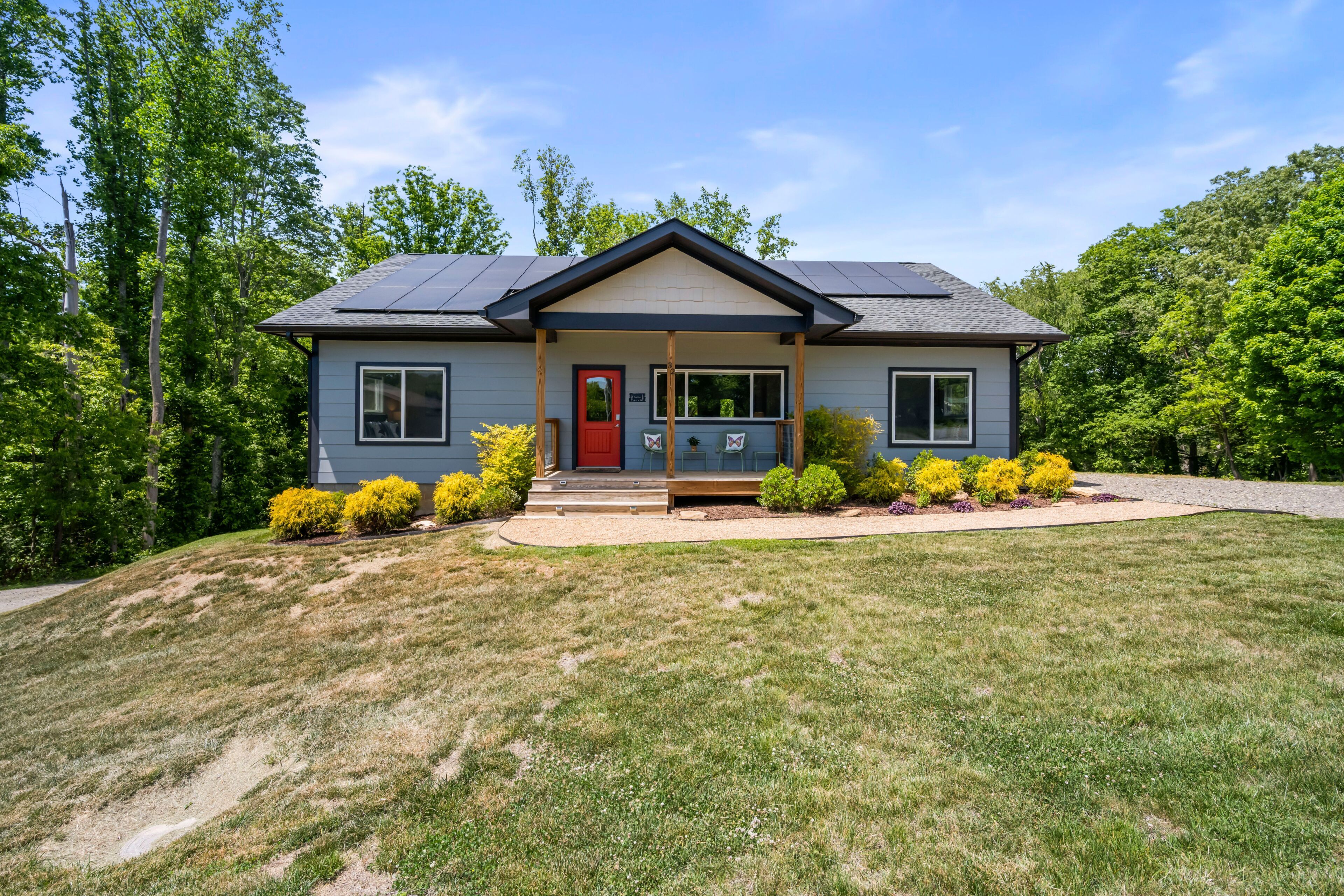 A two-story house with a red door, solar panels, and a front porch.