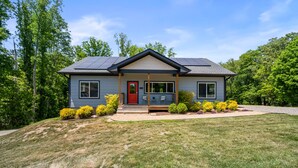 A two-story house with a red door, solar panels, and a front porch. - Fox Den | 4 Suite Retreat + EV | 10 Mins to AVL (Asheville)