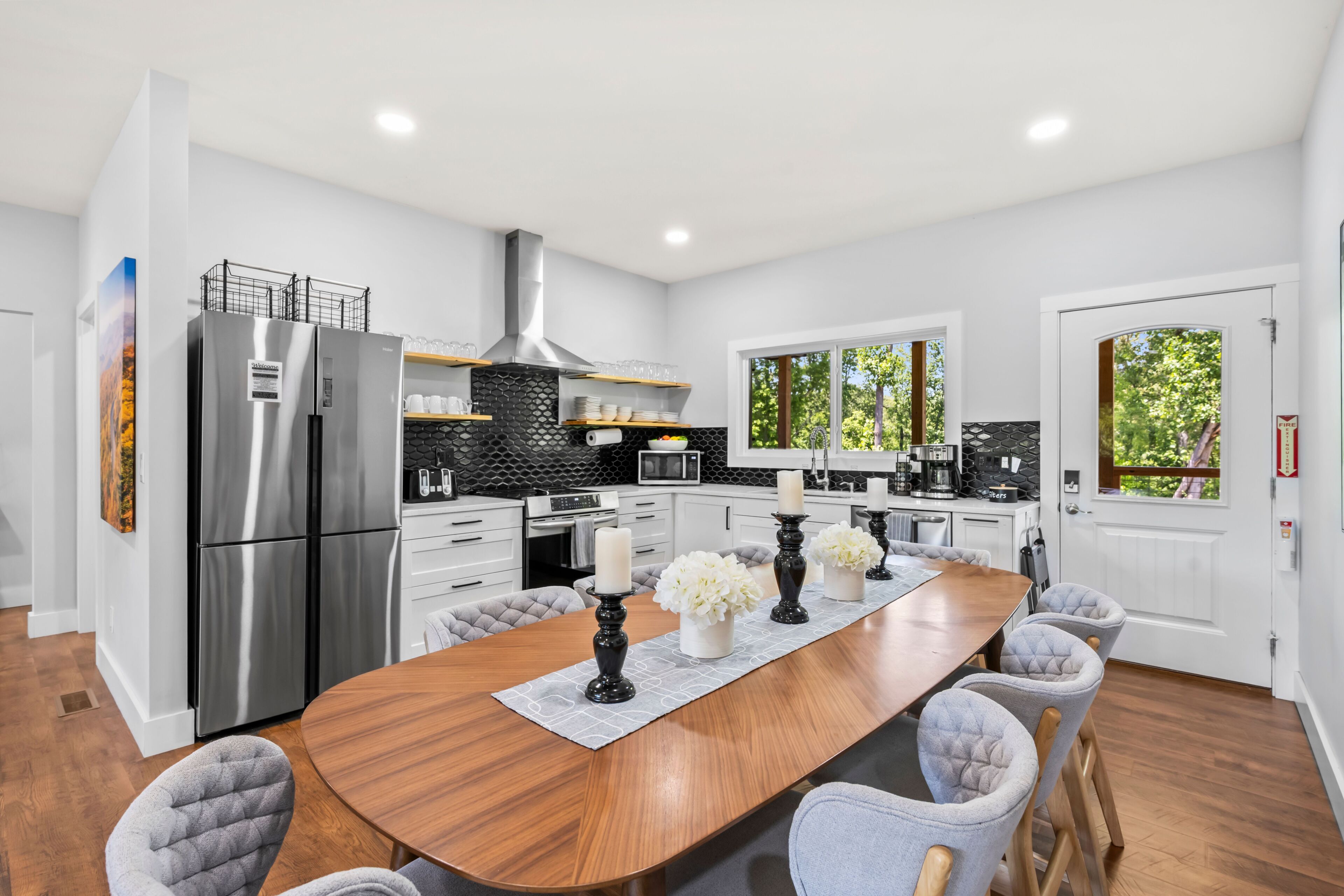 A modern kitchen with a large island, stainless steel appliances, and a view of greenery outside.