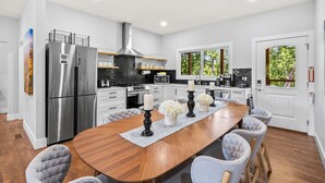 A modern kitchen with a large island, stainless steel appliances, and a view of greenery outside. - Fox Den | 4 Suite Retreat + EV | 10 Mins to AVL (Asheville)