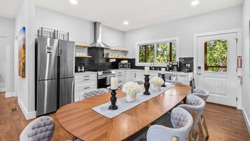 A modern kitchen with a large island, stainless steel appliances, and a view of greenery outside.