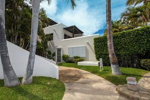 Een modern huis met een betonnen pad dat naar de ingang leidt, omringd door palmbomen en een verzorgd gazon.