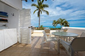 Een balkon met uitzicht op de oceaan, een palmboom en een ronde tafel met stoelen.