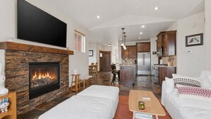 A living room with a fireplace, white sofas, a coffee table, and a TV mounted on the wall. - Ridgeline Retreat with Private Hot Tub (Heber City)