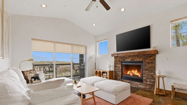 A spacious living room with a fireplace, a large TV, and a balcony with outdoor furniture. - Ridgeline Retreat with Private Hot Tub (Heber City)