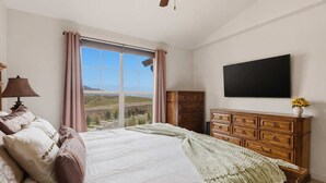A bedroom with a large window, a bed with pillows, a dresser, and a flat-screen TV on the wall. - Ridgeline Retreat with Private Hot Tub (Heber City)