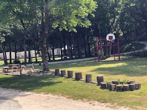Basketballfeld mit Korb, umgeben von Bäumen und einem Picknickplatz.
