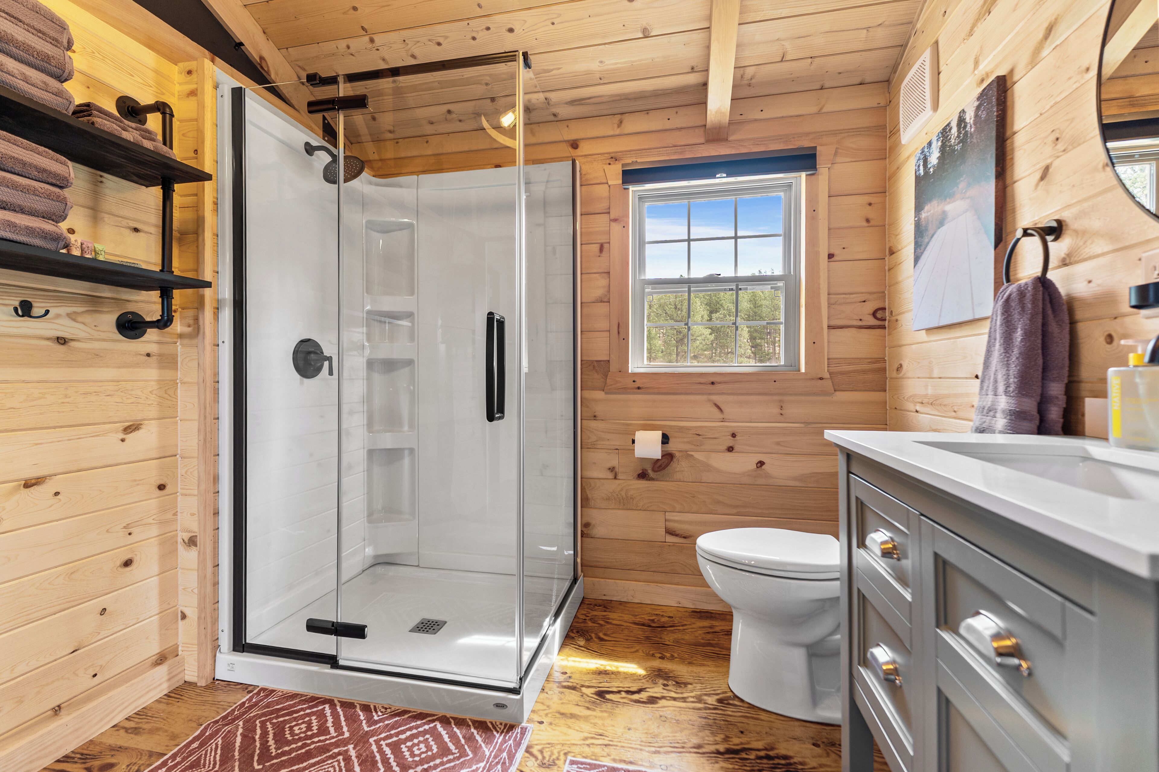 A wooden cabin bathroom with a glass shower enclosure, a toilet, and a sink with a mirror.