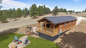 A log cabin with a deck, outdoor seating, and a stone fire pit.