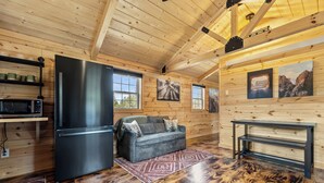 A wooden cabin interior with a kitchen, a sofa, and a dining table.