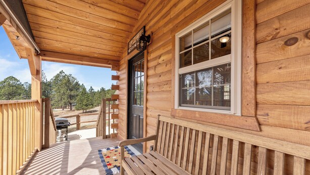 A wooden cabin with a porch, a bench, and a grill.