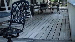En inglasad veranda med trägolv, utemöbler inklusive stolar och ett bord, och utsikt över det omgivande området.