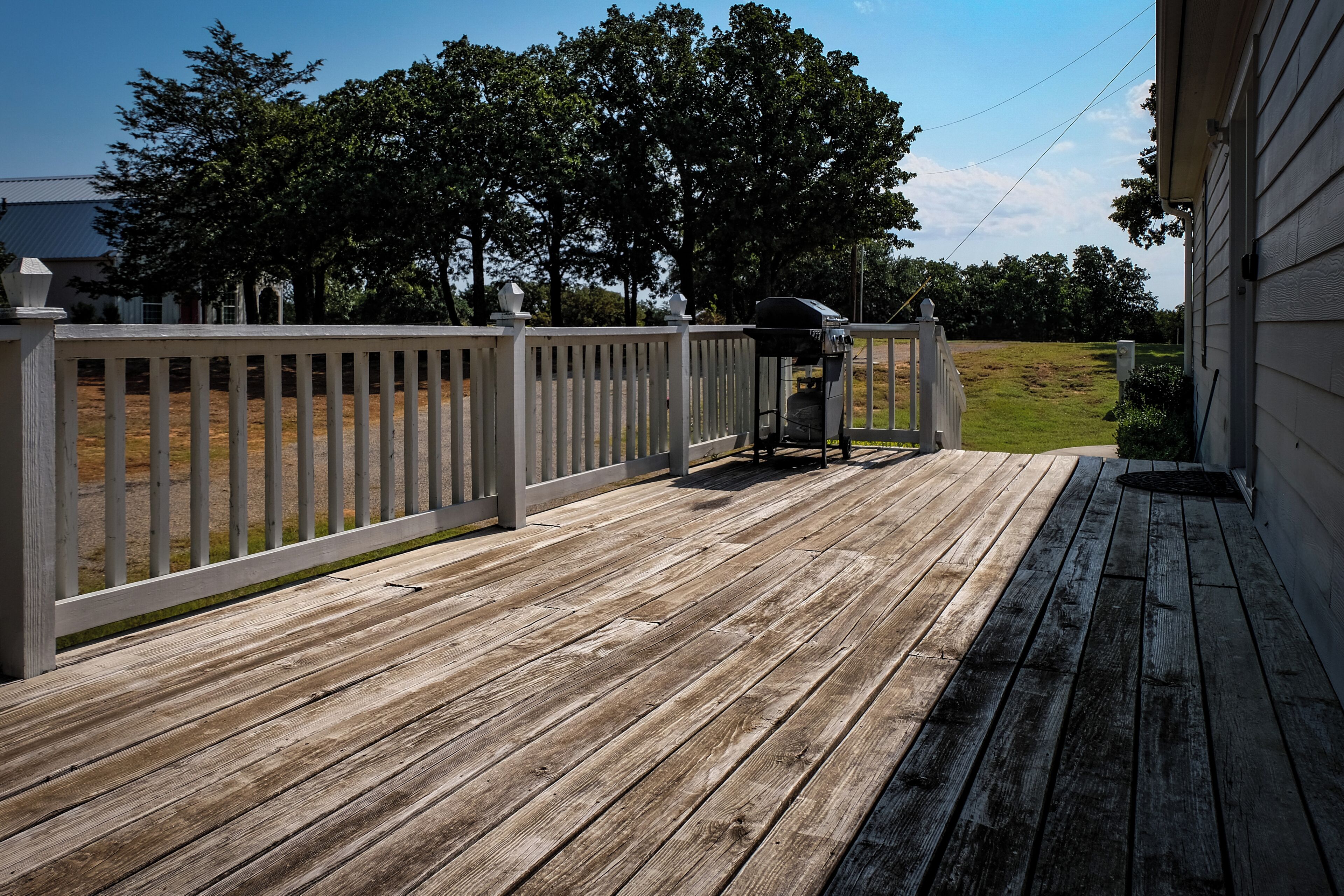 A wooden deck with a barbecue grill, white railing, and a grassy yard in the background.