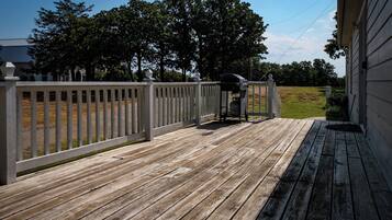 A wooden deck with a barbecue grill, white railing, and a grassy yard in the background.