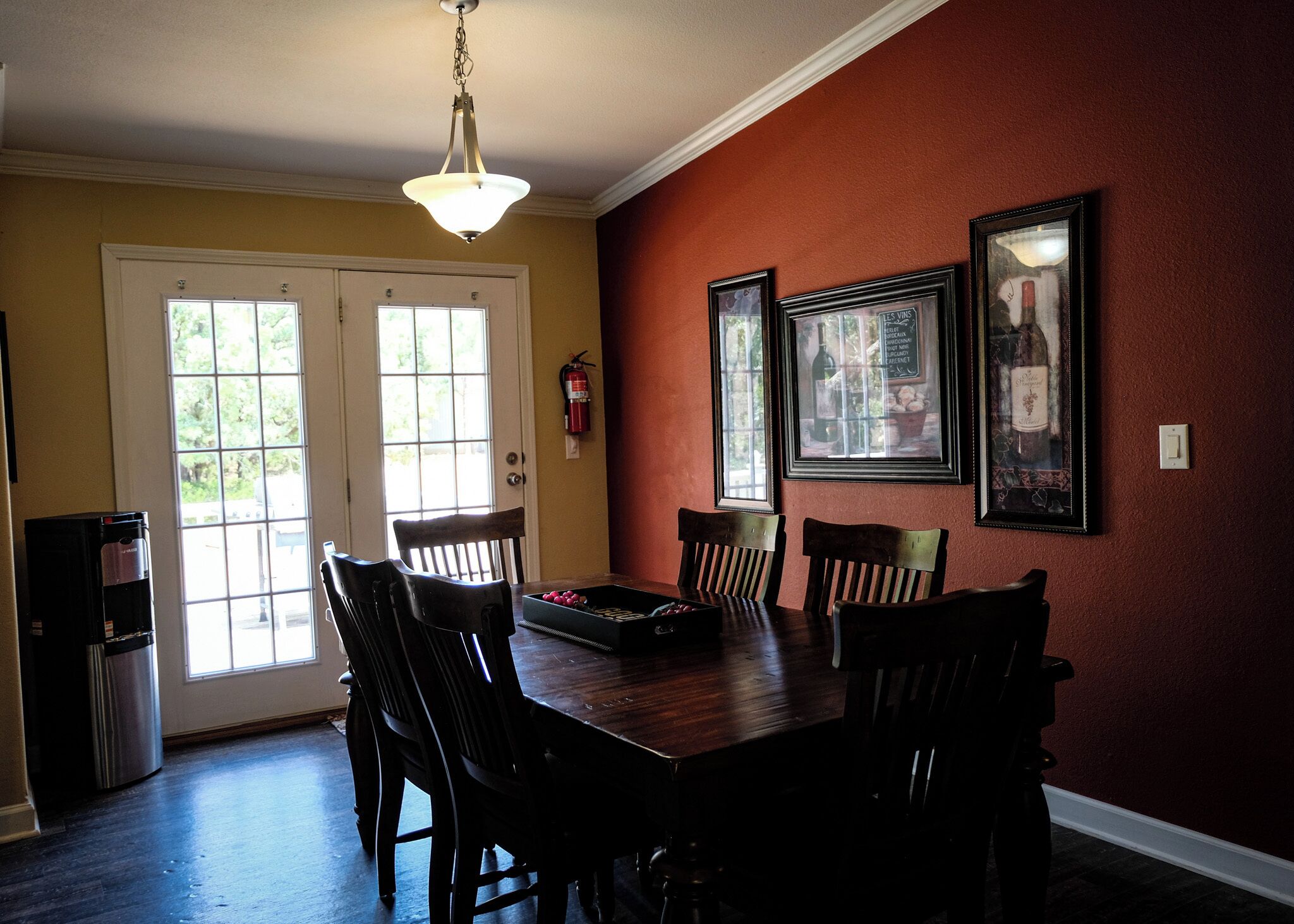 A dining room with a wooden table, chairs, a chandelier, and framed pictures on the wall.