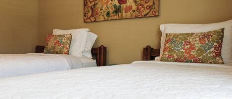 A hotel room with two beds, each with white bedding and floral-patterned pillows.